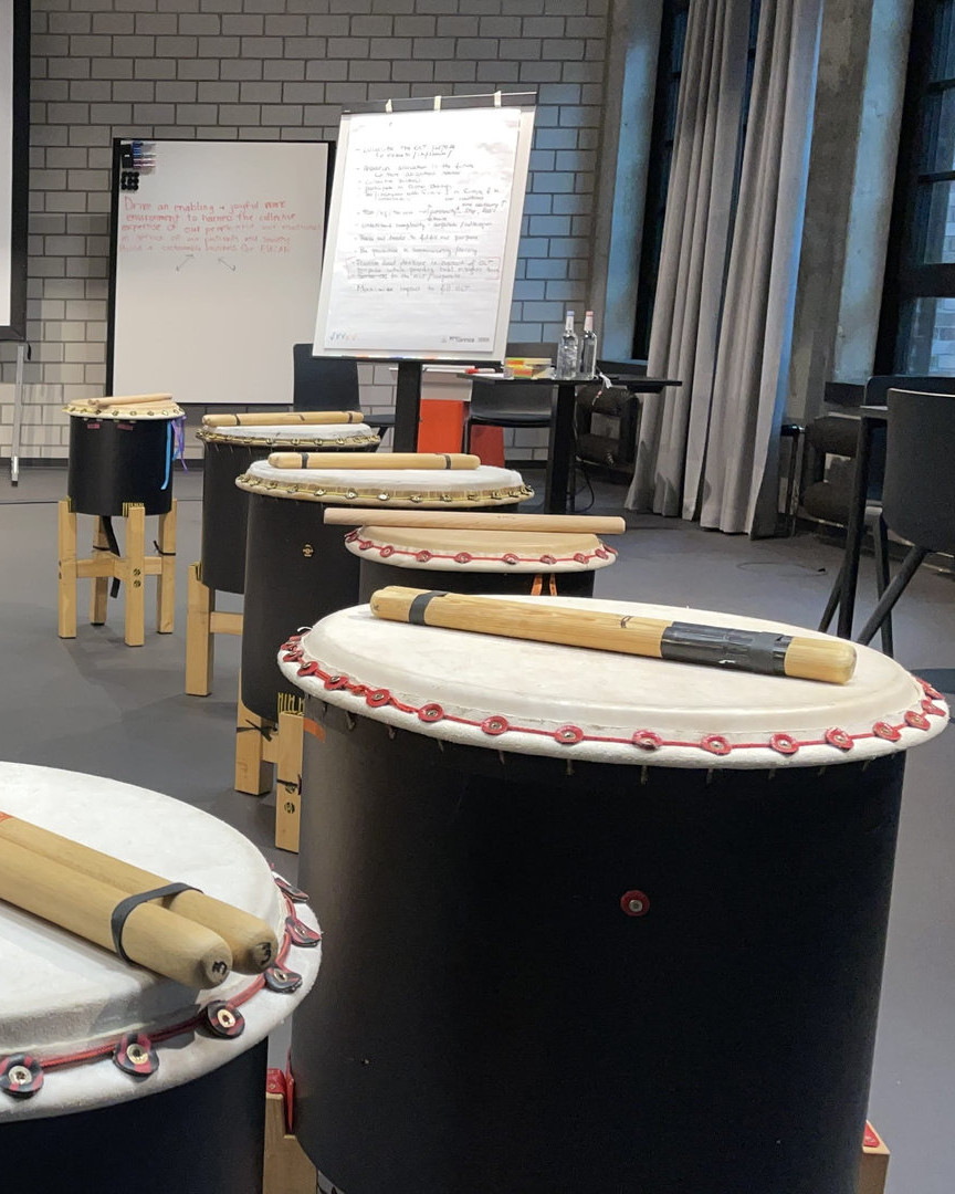 Taiko-Trommeln stehen in einer Reihe bereit, im Hintergrund beschriebene Flipcharts